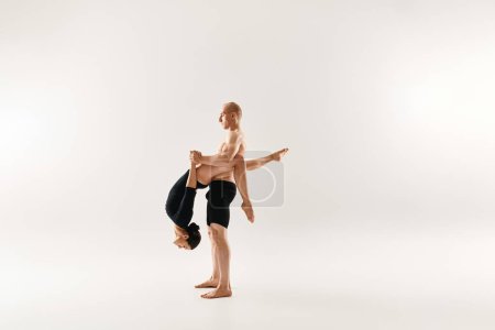 Ein hemdloser junger Mann und eine Frau tanzen mit akrobatischer Anmut, während sie vor weißem Hintergrund in der Luft schweben.