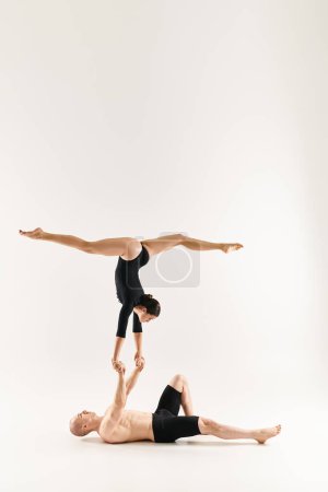 Un joven sin camisa y una bailarina desafían la gravedad en una pose sincronizada sobre un fondo de estudio blanco.