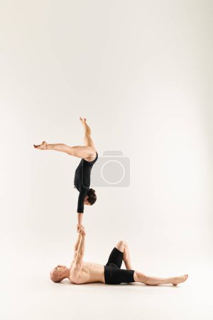 A shirtless young man and a woman gracefully perform a handstand in a studio setting on a white background.