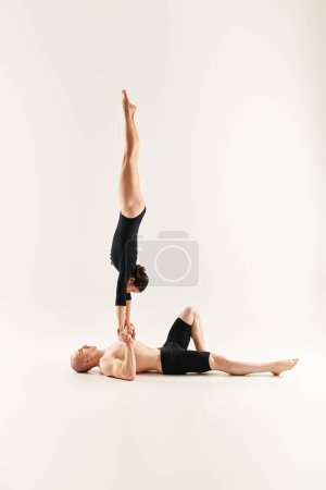 Ein hemdloser junger Mann und eine Frau, die vor weißer Studiokulisse in perfekter Synchronität einen akrobatischen Handstand vollführen.