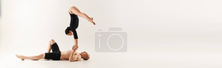 Téléchargez les photos : Un jeune homme torse nu et une femme en couple exécutant un handstand synchronisé dans un décor de studio sur fond blanc. - en image libre de droit