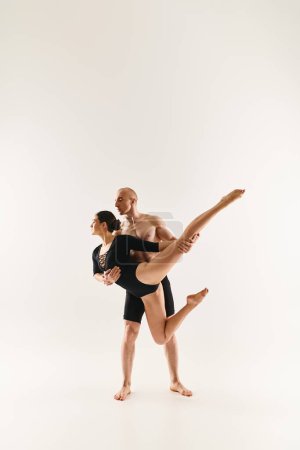 A shirtless young man and a young woman gracefully perform acrobatic elements in a studio setting against a white background.