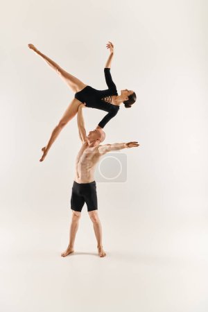 Un joven sin camisa y una joven bailan en el aire, interpretando elementos acrobáticos en un estudio sobre un fondo blanco.