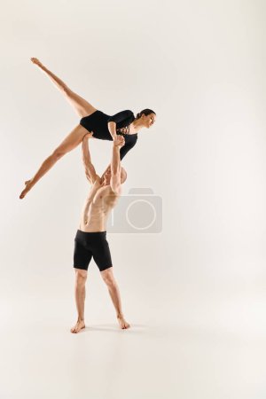 Ein hemdloser junger Mann und eine Frau führen vor weißem Hintergrund einen anmutigen, akrobatischen Tanz auf, der in der Luft schwebt.