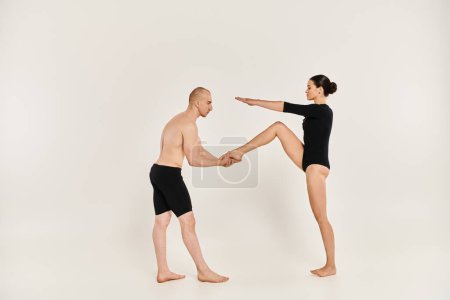 Un jeune homme torse nu et une femme en noir exécutent des mouvements de danse acrobatique en studio.