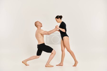 Ein hemdloser junger Mann und eine Frau, die in einem Studio vor weißem Hintergrund komplizierte Tanzpositionen und akrobatische Elemente aufführen.