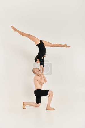 Woman in black performs handstand in perfect synchrony, showcasing their balance and strength on a white studio background.