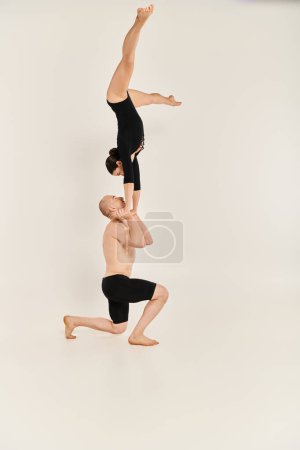 Young shirtless man and woman execute a flawless handstand in mid-air against a white studio backdrop.