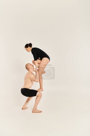 Un joven sin camisa y una mujer ejecutan con elegancia un soporte de mano en un estudio sobre un fondo blanco.