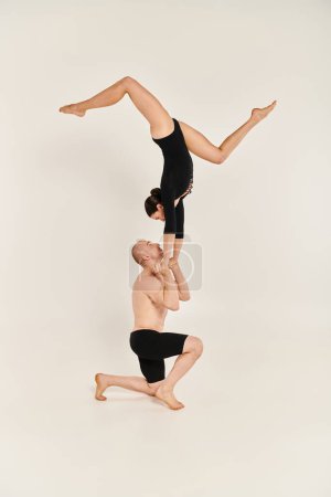 A young shirtless man and woman perform acrobatic handstand in mid-air, showcasing their dance talents against a white backdrop.