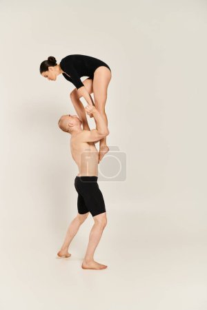 Shirtless young man and woman dancing with acrobatic finesse in a harmonious handstand pose against a white studio backdrop.