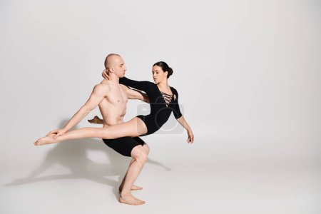 A shirtless young man and a woman in a couple performing graceful and acrobatic dance moves in a studio setting on a white background.