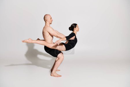 A shirtless young man and a woman dance together, performing acrobatic moves with elegance and agility on a white studio background.