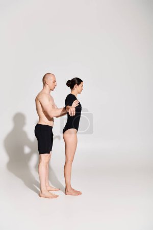 Young man shirtless and woman in black perform acrobatic dance moves in a studio against a white background.