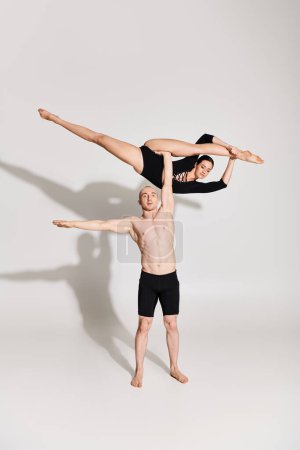 Shirtless young man and woman perform acrobatic element harmony in front of a white background.