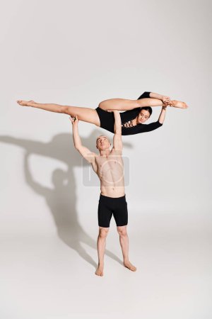 A shirtless young man and a young woman perform a handstand as part of an acrobatic dance routine in a studio setting.