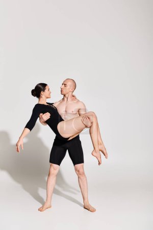 A shirtless young man holds a woman in an acrobatic dance pose, showing strength and grace in a studio setting on a white background.