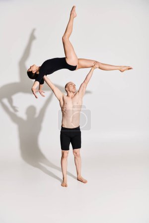 Young shirtless man holding a young woman, showcasing agility and balance in a studio setting against a white background.