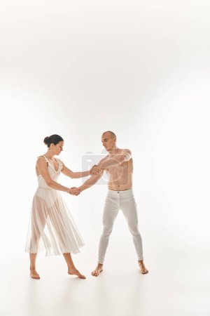 Un jeune homme torse nu et une jeune femme en robe blanche dansent ensemble, exécutant des éléments acrobatiques dans un décor de studio sur fond blanc.
