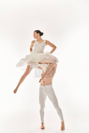 A shirtless man and a woman in a white dress dance together, performing acrobatic elements in a studio setting against a white background.