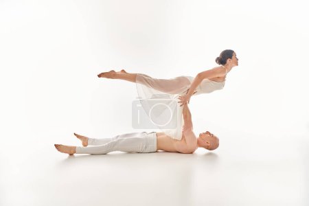 Un joven sin camisa y una mujer con un vestido blanco realizan una rutina de baile elegante y acrobática en un ambiente de estudio.