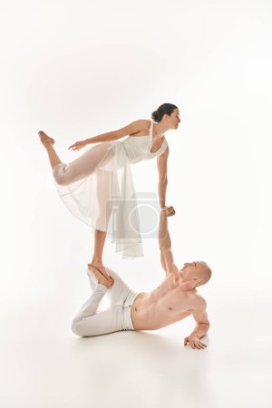 Un jeune homme torse nu et une femme en robe blanche effectuent ensemble des exercices acrobatiques en studio sur fond blanc.
