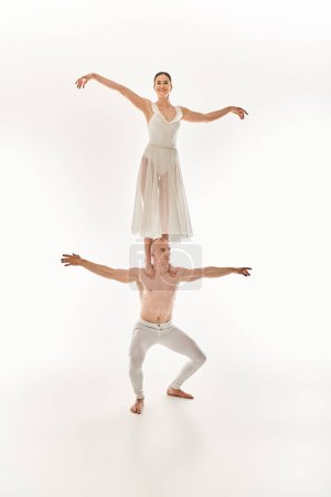 Jeune homme et femme torse nu en robe blanche dansant gracieusement, mettant en valeur l'équilibre acrobatique.