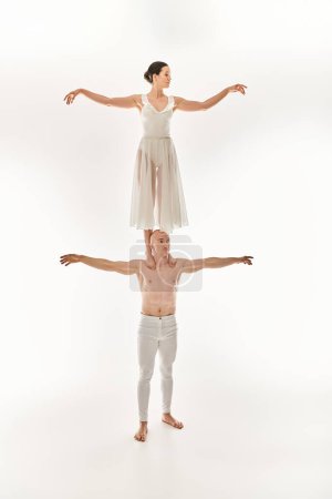 Shirtless young man and woman in white dress showcase acrobatic talent, balancing in a dynamic dance pose.