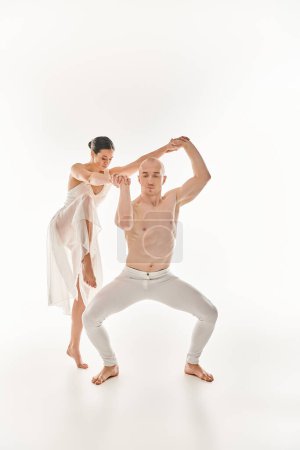 A shirtless young man and a woman in a white dress dance together, performing acrobatic elements in a studio setting against a white backdrop.