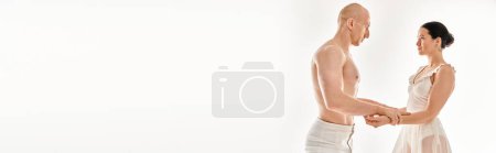 Photo for A young man shirtless and a young woman in a white dress perform acrobatic elements while dancing together in a studio against a white background. - Royalty Free Image