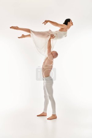 Shirtless young man and woman in white dress execute acrobatic dance moves in a captivating studio shot on a white background.