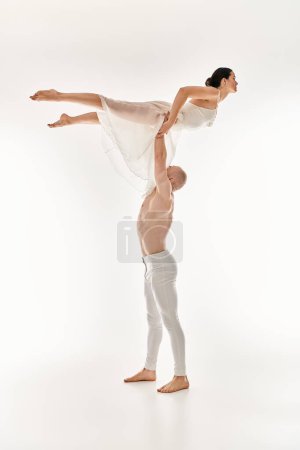 A shirtless young man and a woman in a white dress perform a dynamic and acrobatic dance routine in a studio setting.