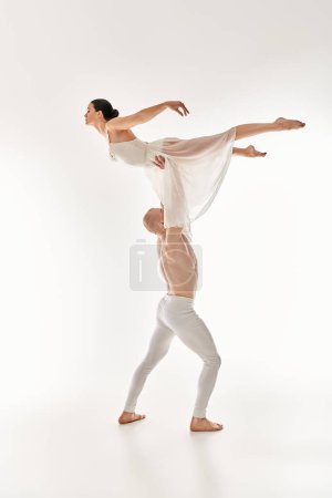 Ein hemdloser junger Mann und eine Frau in einem weißen Kleid tanzen anmutig zusammen und integrieren akrobatische Elemente vor einer weißen Studiokulisse..