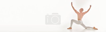 Photo for A young man unleashes his acrobatic skills, joyfully dancing with arms raised in the air against a white studio backdrop. - Royalty Free Image