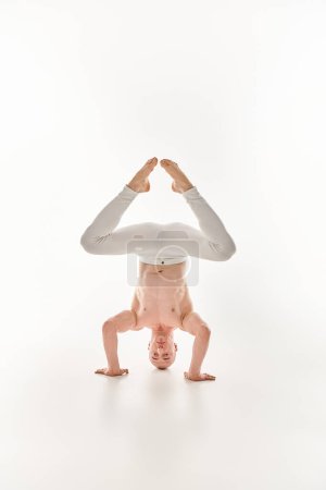 Ein junger Mann demonstriert seine akrobatischen Fähigkeiten mit einem Kopfstand, der in einem Studio vor weißem Hintergrund eingefangen wurde.