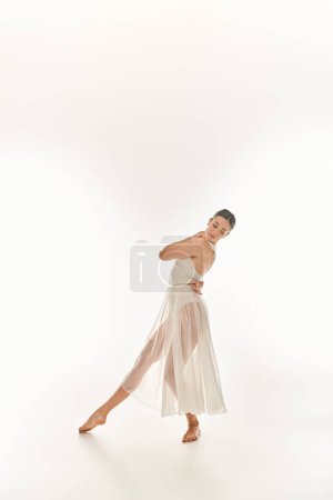 Eine junge Frau tanzt anmutig in einem langen weißen Kleid, verströmt Eleganz und Gelassenheit in einem Studio vor weißem Hintergrund.