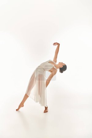 Graceful young woman in flowing white attire performs a perfect handstand in a studio setting against a clean white backdrop.
