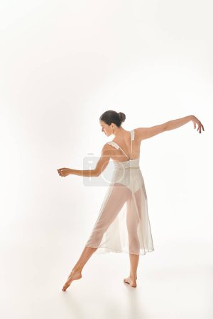 Mujer joven baila con gracia en un vestido blanco largo, exudando belleza y elegancia en un entorno de estudio sobre un fondo blanco.