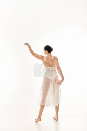 A young woman mesmerizingly dancing in her long white dress against a white background.