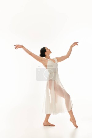 Una joven elegante baila en un vestido blanco que fluye sobre un fondo de estudio blanco.