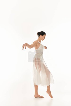 A young woman gracefully dances in a flowing white dress on a white background in a studio setting.