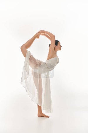 Young woman in a flowing white dress gracefully performing a yoga pose in a serene studio setting.