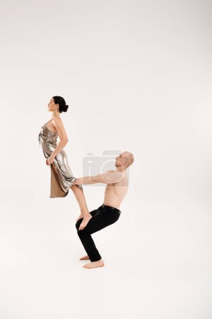 A shirtless man and a woman in a shiny dress doing acrobatic element in a studio setting.