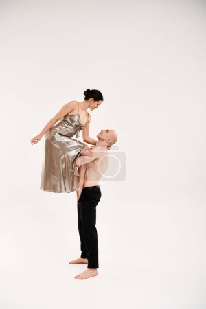 A shirtless young man and a woman in a shiny dress dance performing acrobatic elements. Studio shot on a white background.
