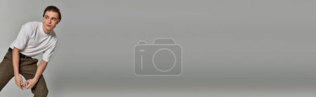 Foto de Hombre de moda en pantalones marrones posando atractivamente sobre fondo gris y mirando hacia otro lado, pancarta - Imagen libre de derechos