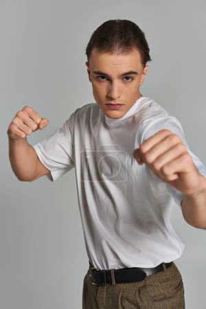 good looking male model in debonair attire posing with fists in front of camera on gray backdrop