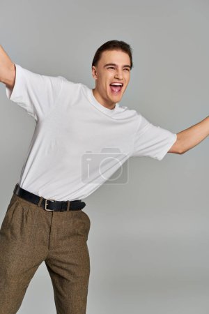joyous elegant male model in stylish attire posing in motion and looking away on gray backdrop