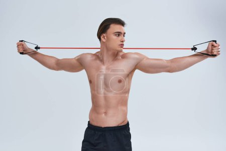 Photo for Alluring shirtless sporty young man in black pants training with fitness expander and looking away - Royalty Free Image