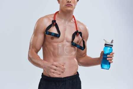 Photo for Cropped view of sexy athletic man in black pants posing topless with bottle and fitness expander - Royalty Free Image