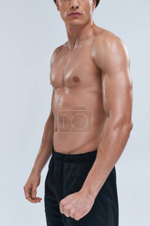 Ausgeschnittene Ansicht des verlockenden jungen athletischen Mannes in schwarzer Hose, der oben ohne auf grauem Hintergrund posiert